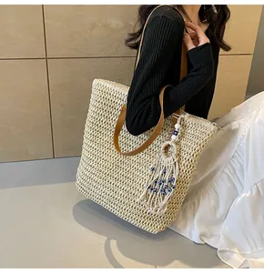 Detail of cream straw tote bag featuring brown leather handles and evil eye tassel charm