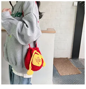 Close-up of red crochet drawstring bag featuring Fu character embroidery and pom-poms