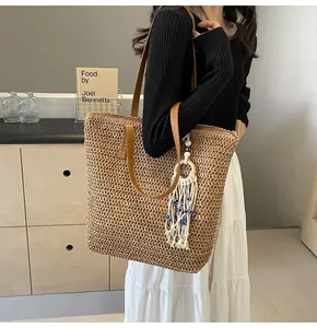 Detail of woven straw tote bag with brown leather straps and blue evil eye tassel charm