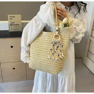 Close-up of a straw tote bag with a boho tassel and evil eye bead charm on a white dress