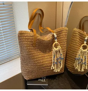 Detail of woven straw tote bag featuring brown leather handle and evil eye tassel charm