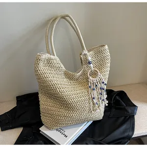 Detail of woven beach tote with blue evil eye tassel charm on a neutral background