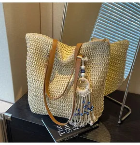 Close-up of woven tote bag with brown faux leather straps and evil eye tassel detail