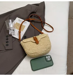 Détail d'un sac besace en paille tressée avec bandoulière en cuir brun et boucles dorées