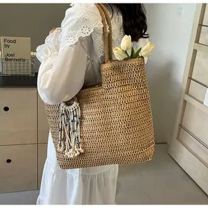 Close-up of handwoven straw tote bag with boho tassel detail and fresh white tulips