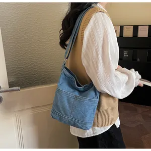 Détail du sac seau en denim bleu avec deux poches avant et bandoulière réglable