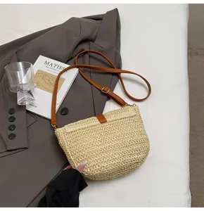 Gros plan d'un sac selle en paille tressée avec bandoulière en cuir brun sur tissu doux