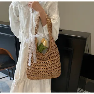 Détail d'un sac bandoulière en paille ajourée avec ruban en dentelle blanche et tulipes