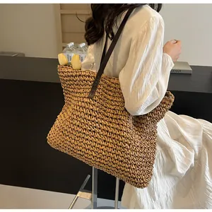 Detail of large woven straw tote with dark brown leather straps on a model in white dress