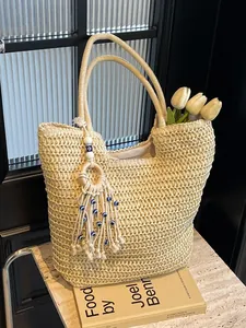 Beige woven beach tote bag with fringe evil eye charm and top handles for summer fashion