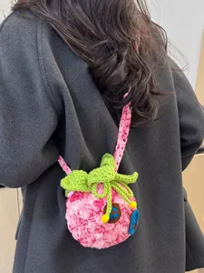 Pink crochet house crossbody bag with green leaf detail on a grey coat background