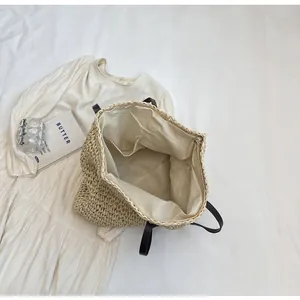 Detail view of large straw tote bag with black leather handle and inner pocket lining