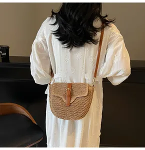 Détail d'un sac besace en paille tressée avec lanière en cuir porté sur robe blanche