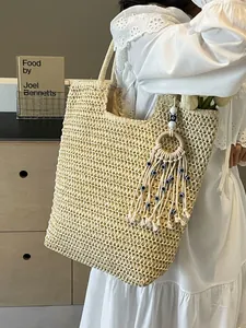 Chic beige woven straw tote bag with evil eye tassel shown on a shoulder of a model
