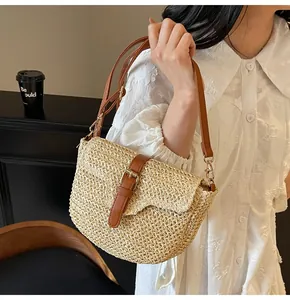 Détail du tissage en paille beige et de la bandoulière en cuir marron du sac de plage