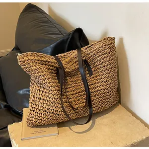 Detail of a large straw tote bag featuring brown shoulder straps and a top zipper closure