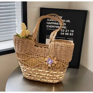 Dettaglio della borsa tote in paglia intrecciata con bordi ondulati e charm a farfalla