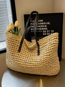 Large straw woven tote bag with brown leather straps on a cafe table with tulips