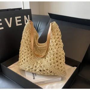 Detail of hollow-out straw woven bag with contrast brown leather handles on black background