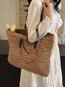 Large woven straw tote bag with brown leather handles worn by a model in a summer style