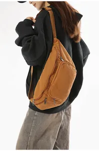 Close-up of tan canvas chest bag with multi-zipper compartments on a male model