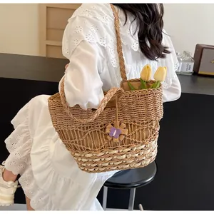 Dettaglio della borsa tote in paglia con ciondolo a fiore viola portata da donna in abito