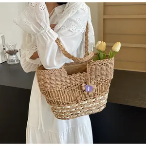 Dettaglio di borsa tote in paglia intrecciata a mano con ciondolo a farfalla e tulipani