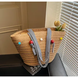 Detailed close-up of woven straw tote bag with colorful pom-poms and striped handles