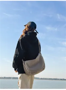Large canvas messenger bag shown on model in an outdoor lake setting for a casual lifestyle