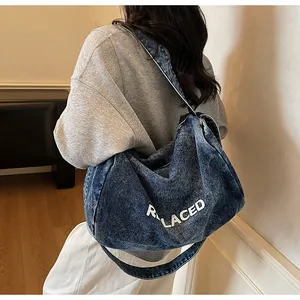 Detail of large denim crossbody bag with white REPLACED lettering and washed texture