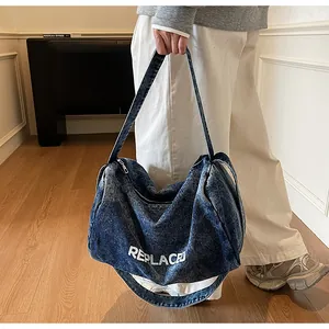 Detail of blue denim hobo bag showing the white REPLACED print and washed texture