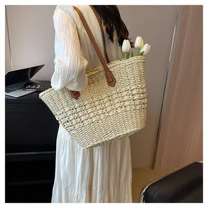 Detail view of woven straw tote bag with brown leather straps and intricate textures