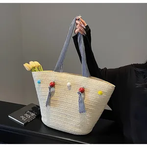Detail of straw tote bag with striped handles, colorful pom-poms, and summer casual style