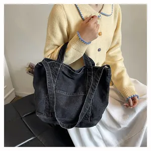 Detail of washed black denim tote bag featuring white contrast stitching and dual handles