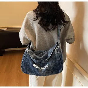 Macro view of blue washed denim hobo bag with white REPLACED text worn by a model