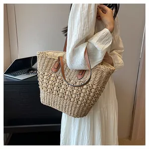 Detail view of woven straw tote bag with brown leather handles worn by a model