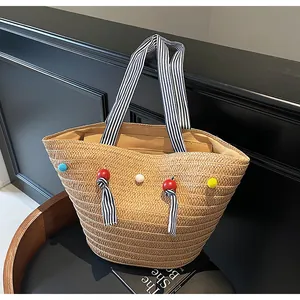Detail of straw tote bag featuring colorful pom-poms and black white striped cloth handles