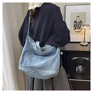 Detail of light blue denim tote bag showing stitching and front pocket in lifestyle setting