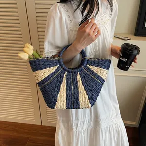 Detail of fan-shaped straw bag featuring navy stripes and delicate gold thread accents