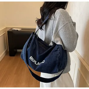 Detail of a dark blue denim crossbody bag with white REPLACED letters and a wide strap
