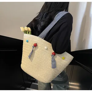 Detail of a woven straw tote bag with striped shoulder straps and colorful pompom charms