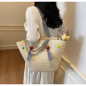 Detail of straw tote bag featuring colorful pompoms and striped ribbon bow handles