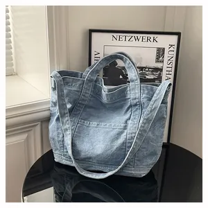 Detail of light blue washed denim tote bag showing the front pocket and sturdy double handles