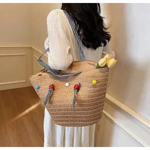 Detail of spacious straw tote bag with colorful pom-poms and striped shoulder straps