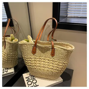 Detail of the woven texture and brown leather strap on a beige summer straw tote bag