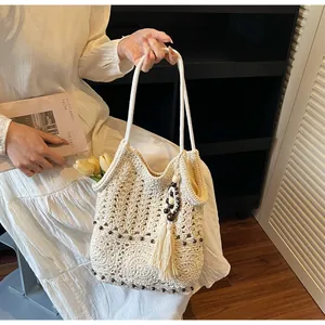 Nahaufnahme der cremefarbenen Stricktasche mit floralem Häkelmuster und Quastenanhänger