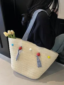 Large straw tote bag with colorful pom-poms and striped straps for beach vacations