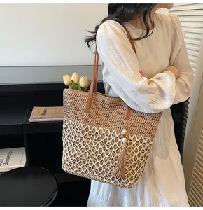 Détail du sac cabas en paille tressée avec lanières en cuir marron et pompon décoratif
