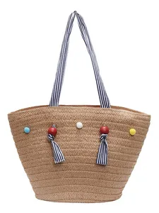 Large straw tote bag with striped handles and colorful decorative pom-poms for beach