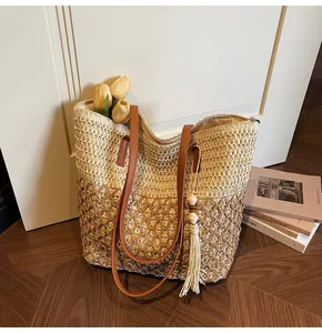 Détail d'un sac cabas en paille tissée bicolore avec sangles en cuir et pompon décoratif